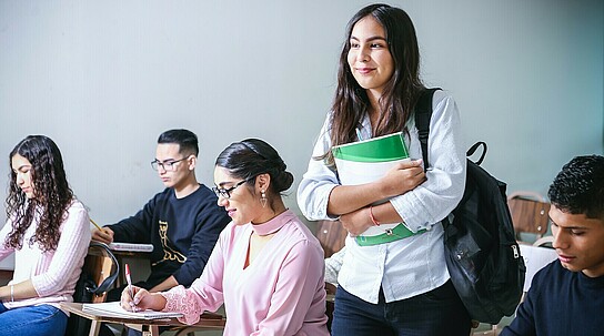 Junge Frau mit Heft unterm Arm im Klassenzimmer