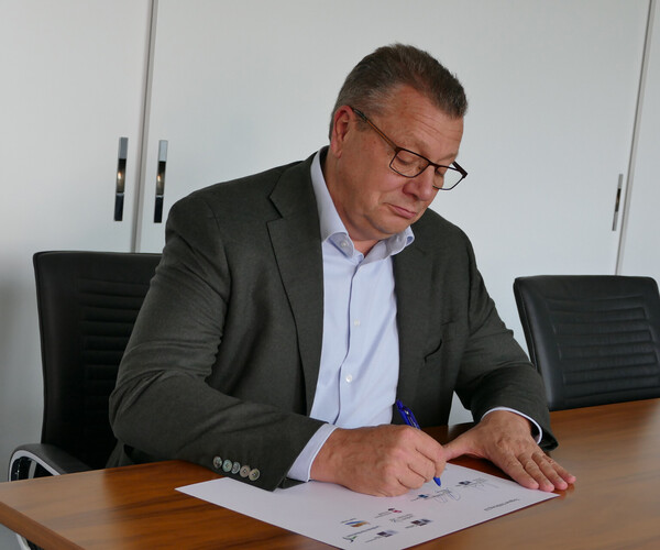 Kristian Kirpal, Präsident der IHK zu leipzig, sitzt an einem Tisch und unterzeichnet ein Schriftstück. 