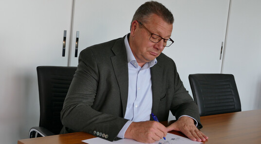 Kristian Kirpal, Präsident der IHK zu leipzig, sitzt an einem Tisch und unterzeichnet ein Schriftstück. 