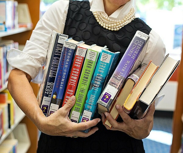Mann trägt viele Bücher in der Bibliothek mit sich herum