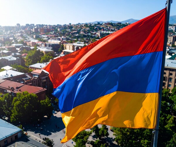 Flagge Armeniens (Streifen untereinander in rot-blau-gelb), dahinter eine Stadt