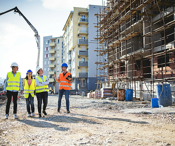 vier Bauarbeiter laufen neben einer Baustelle