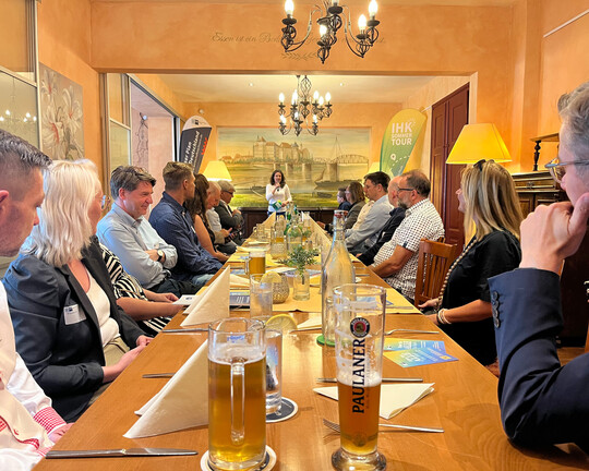 Impressionen der IHK-Sommertour 2025 in Werdau/Torgau: Unternehmer und ihK-Mitarbeitenden sitzen an einem langen Tisch und hören Moderatorin Melanie Nolte zu