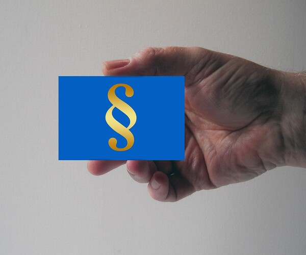 Hand hält Kärtchen mit Paragrafen-Symbol