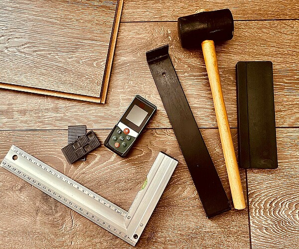 Werkzeuge um Bodenbelag einzubauen, wie Hammer und Lineal, liegen auf dem Boden