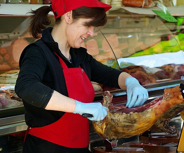 Metzgerin schneidet ein Stück Fleisch ab