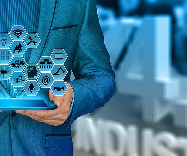 Mann hält Tablet das Logos projiziert in der Hand und steht vor einem 4.0 Industrie Logo