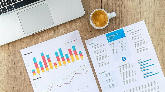 Statistiken auf Papier neben Rechner und Kaffeetasse