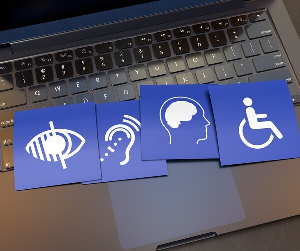 Symbolbild: Digitale Barrierefreiheit. Kärtchen mit unterschiedlichen Symbole für Einschränkungen liegen auf der Tastatur von einem Laptop