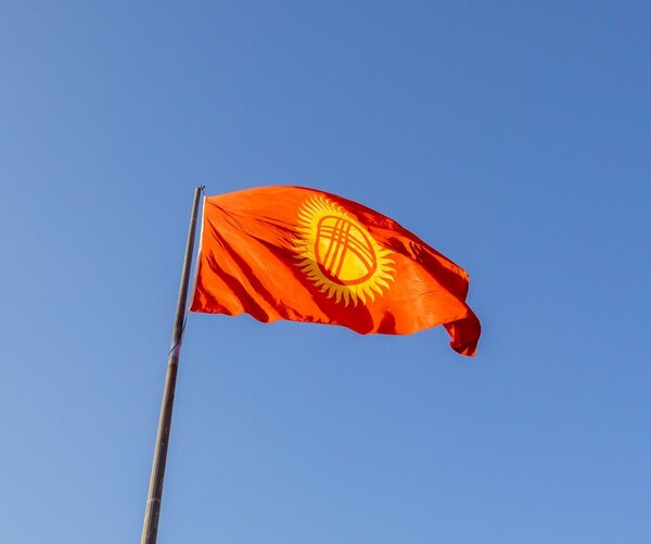 Fahne von Kirgisistan wedelt im Wind. Rote Fahne mit einer Art gelben Sonne in der Mitte.