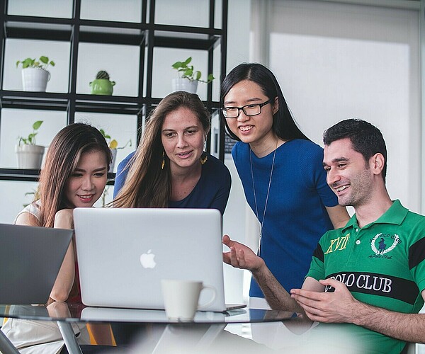 Vier Menschen schauen gemeinsam auf einen Laptop