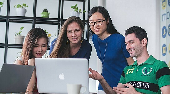 Vier Menschen schauen gemeinsam auf einen Laptop