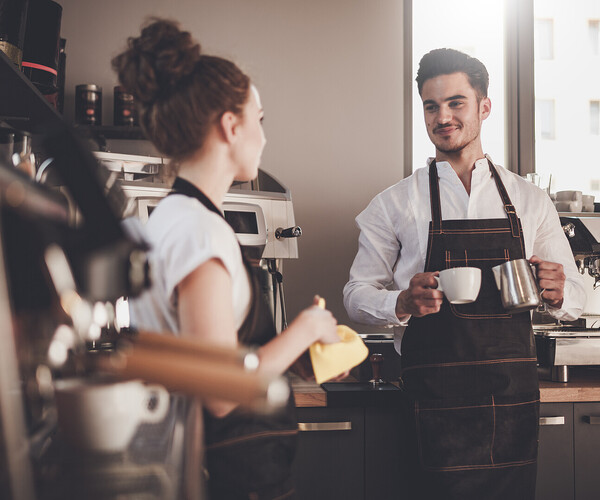 Gastronomiearbeiter unterhalten sich neben den Kaffeemaschinen