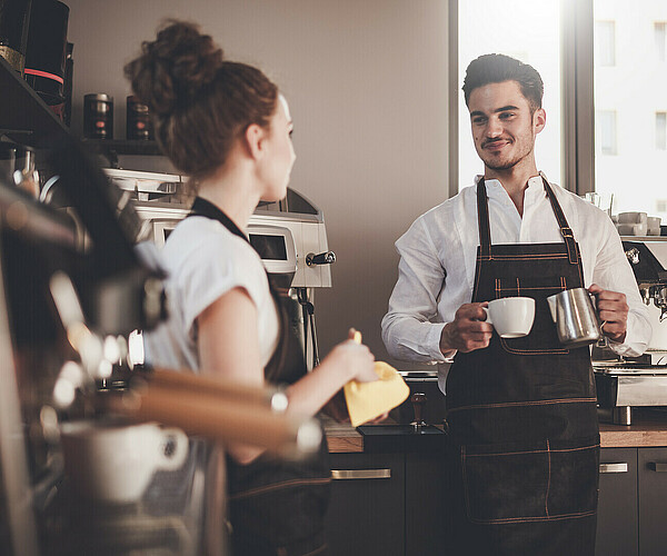 Gastronomiearbeiter unterhalten sich neben den Kaffeemaschinen