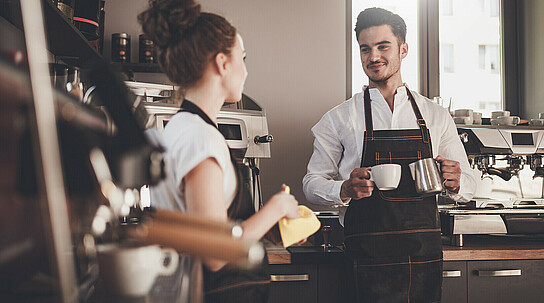 Gastronomiearbeiter unterhalten sich neben den Kaffeemaschinen