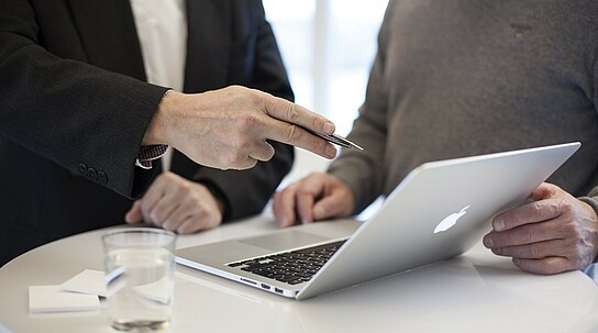 zwei Personen unterhalten sich während sie auf ein Laptop schauen