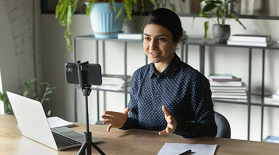 Successful Indian businesswoman recording webinar, using smartphone on tripod