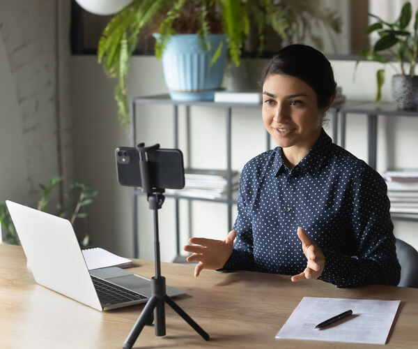 Successful Indian businesswoman recording webinar, using smartphone on tripod