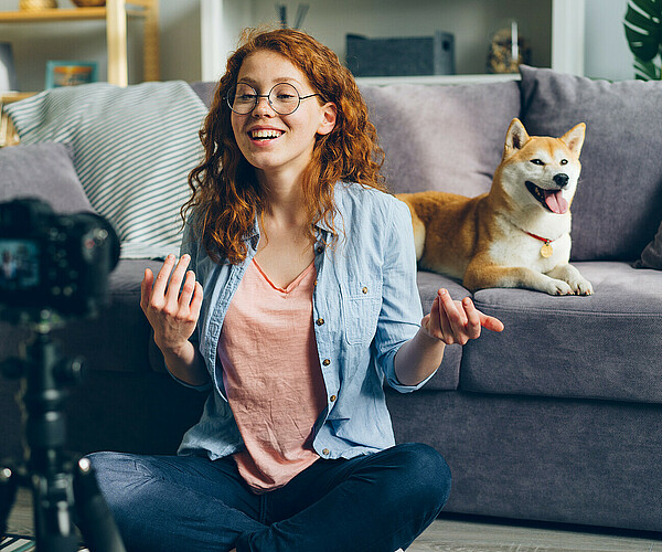 Beautiful blogger and cute dog recording video using camera at home talking