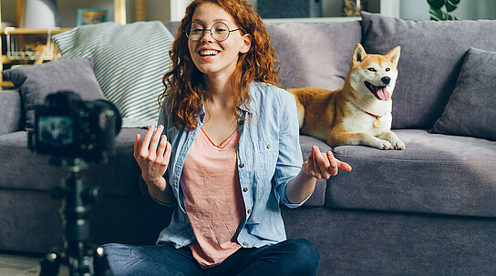 Beautiful blogger and cute dog recording video using camera at home talking