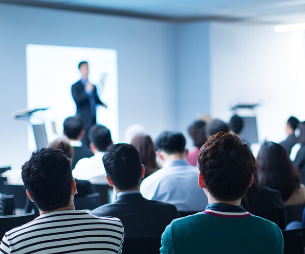 Presenter Presenting on Stage at Conference Meeting. Professional Lecture. Blurred De-focused Unidentifiable Presenter and Audience. Corporate Executive Manager Speaker. People Attendees Veranstaltung Präsenz