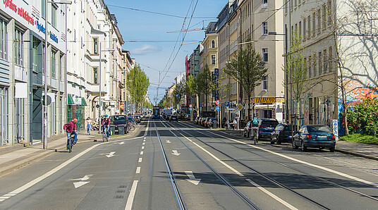 Eisenbahnstraße in Leipzig mit Straßenbahnschienen, parkenden Autos, Fahrradfahrern und Fußgängern