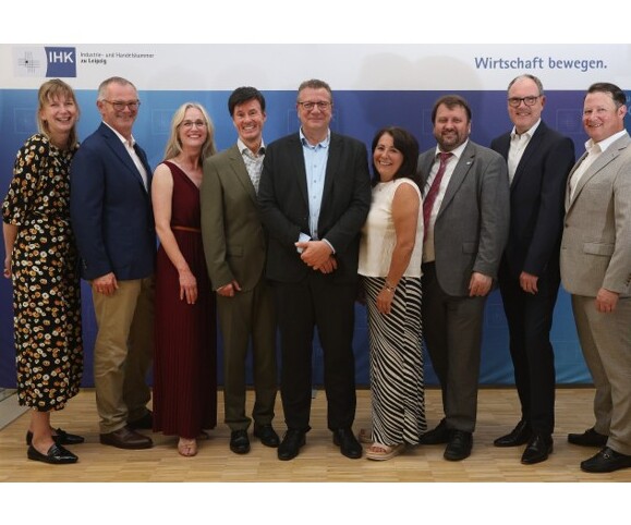 Neun Personen stehen nebeneinander vor einer blauen IHK-Leipzig-Wand mit Logo und dem Schriftzug „Wirtschaft bewegen.“ und tragen Businesskleidung.