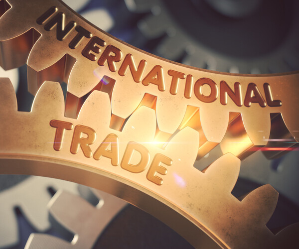 Nahaufnahme zweier ineinandergreifender Zahnräder aus Metall mit der Prägung „INTERNATIONAL TRADE“, symbolisch für globale Wirtschaft und Zusammenarbeit.