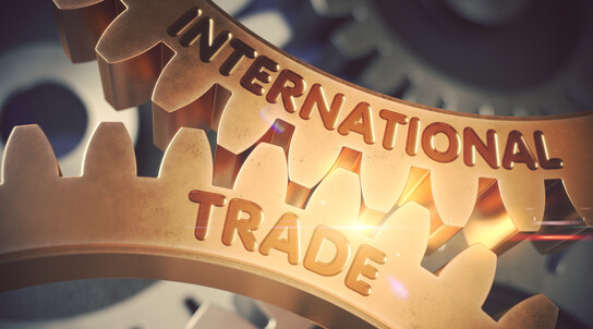 Nahaufnahme zweier ineinandergreifender Zahnräder aus Metall mit der Prägung „INTERNATIONAL TRADE“, symbolisch für globale Wirtschaft und Zusammenarbeit.