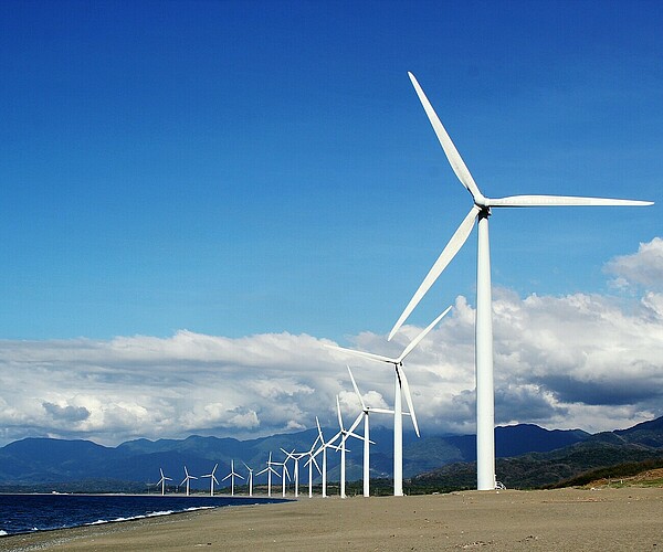 Reihe von Windräderm mit blauem Himmel, Wolken und Bergen im Hintergrund