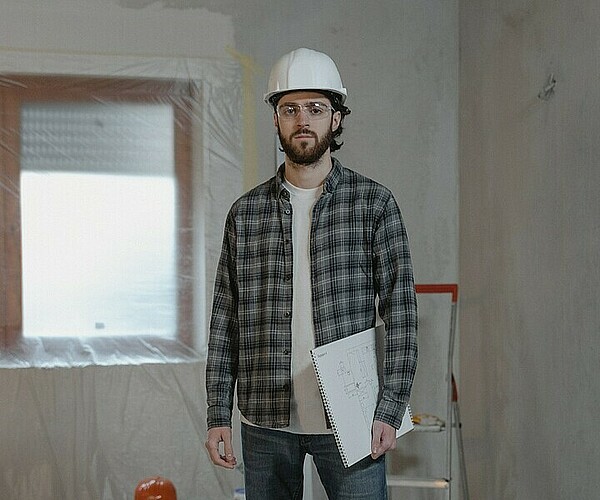 Man mit Plastikhelm steht in einem Zimmer, das gebaut oder saniert wird