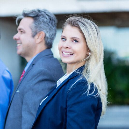 eine Frau steht vor zwei älteren Herren, alle im Business-Look