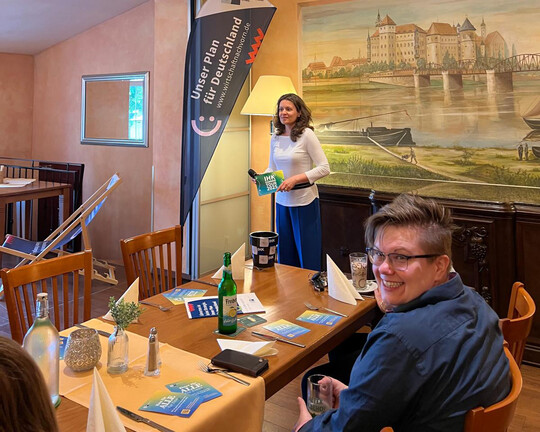 Impressionen der IHK-Sommertour 2025 in Werdau/Torgau: Moderatorin Melanie Nolte spricht. Eine Unternehmerin schaut über ihre Schulter in die Kamera und lacht