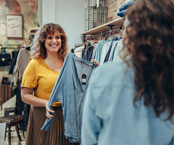 Verkäuferin zeigt Frau Klamotten im Klamottenladen