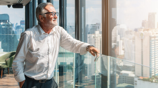älterer Businessmann schaut aus dem Büro auf die Stadt