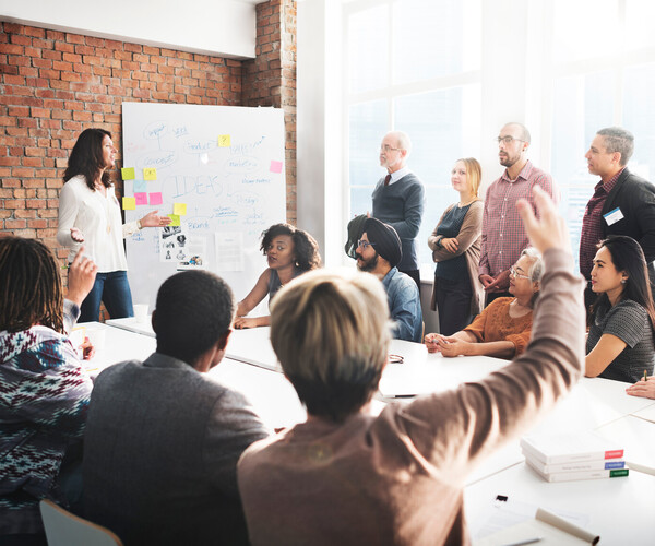 Menschen in einem Workshop arbeiten am Tisch und einige heben die Hand