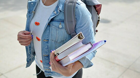 Ausschnitt eines weiblichen Oberkörpers mit Büchern unterm Arm