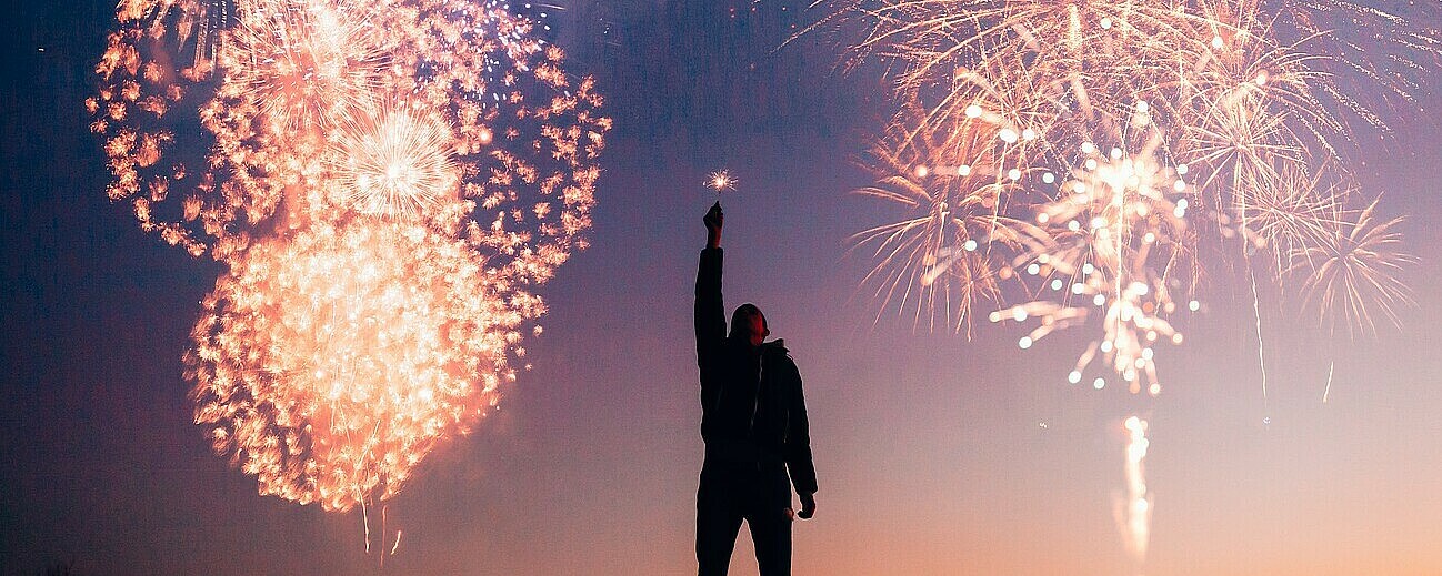 Man zündet Wunderkerze im Freien mit Feuerwerk im hintergrund