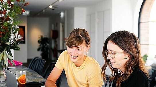 zwei Frauen unterhalten sich und schauen auf einen Laptop