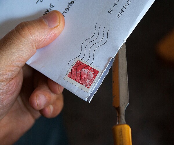 Brief mit Briefmarke wird geöffnet mit Brieföffner