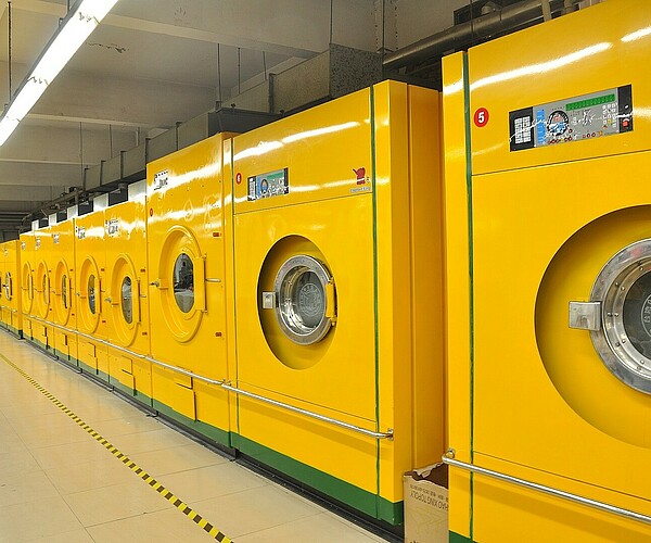 viele gelbe Waschmaschinen stehen nebeneinander in einer Halle