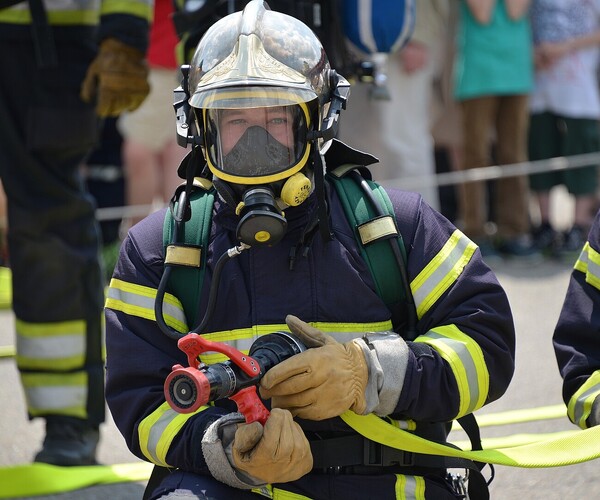 Feuerwehrmann hält Wasserschlauch und guckt in die Kamera