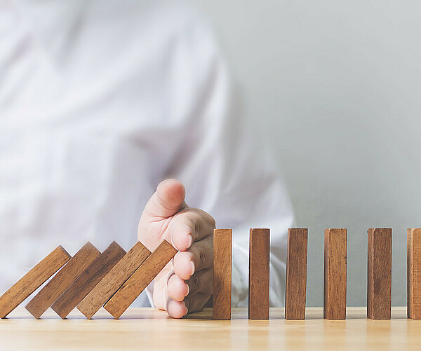 Hand stopping wooden domino business crisis effect or risk protection concept