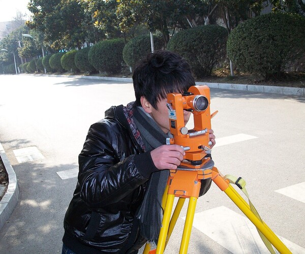 Frau steht mit Messgerät am Straßenrand und guckt durch die Linse auf die Straße