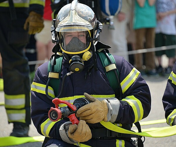 Feuerwehrmann hält Wasserschlauch und guckt in die Kamera