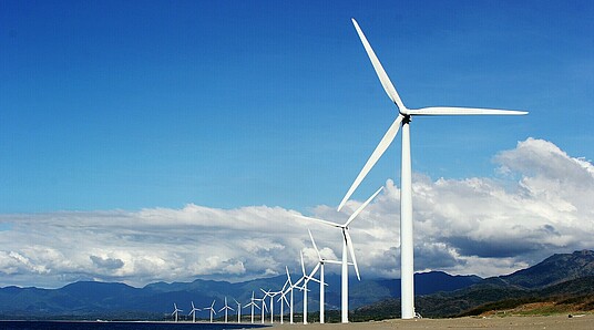 Reihe von Windräderm mit blauem Himmel, Wolken und Bergen im Hintergrund