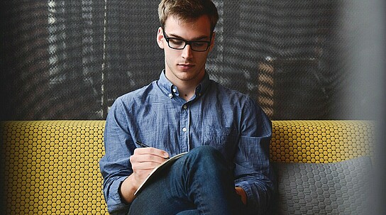 Mann sitzt auf Couch und macht Notizen