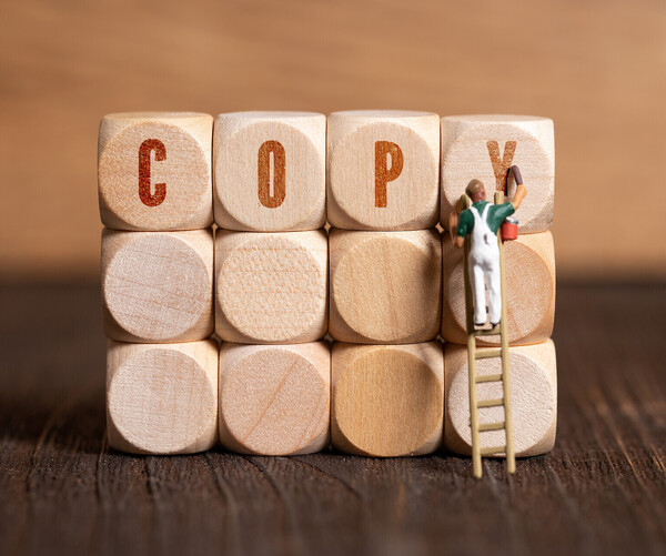 Männchen auf Leiter malt "COPY" auf riesigen Holzwürfel
