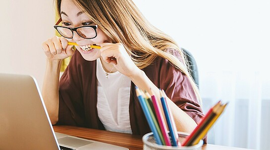 Mädchen kaut auf Bleistift am Laptop