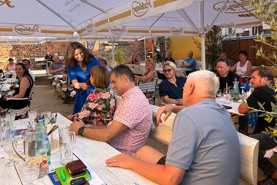 IHK-Sommertour 2025: Menschen sitzen unter Sonnenschirmen auf einer Terrasse und sprechen mit der Moderatorin.